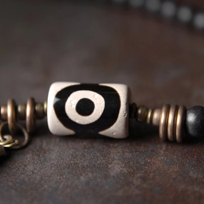 Horizontal close-up view of single-eye agate dzi bead with bronze metal spacers on rustic surface