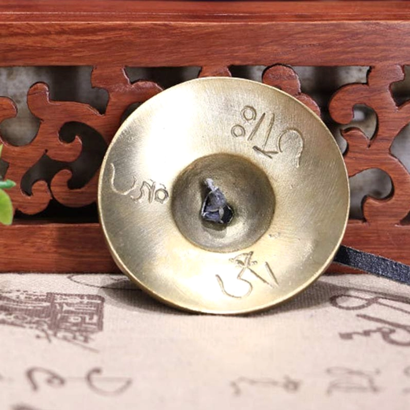Close-up single tingsha brass bell showing central hole and detailed engraved mantras