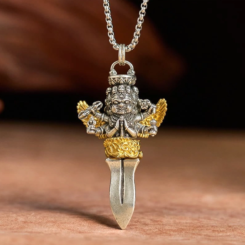Antique silver and gold vajra copper necklace pendant front direct view, displaying intricate carved texture on six-armed deity figure against light wooden background