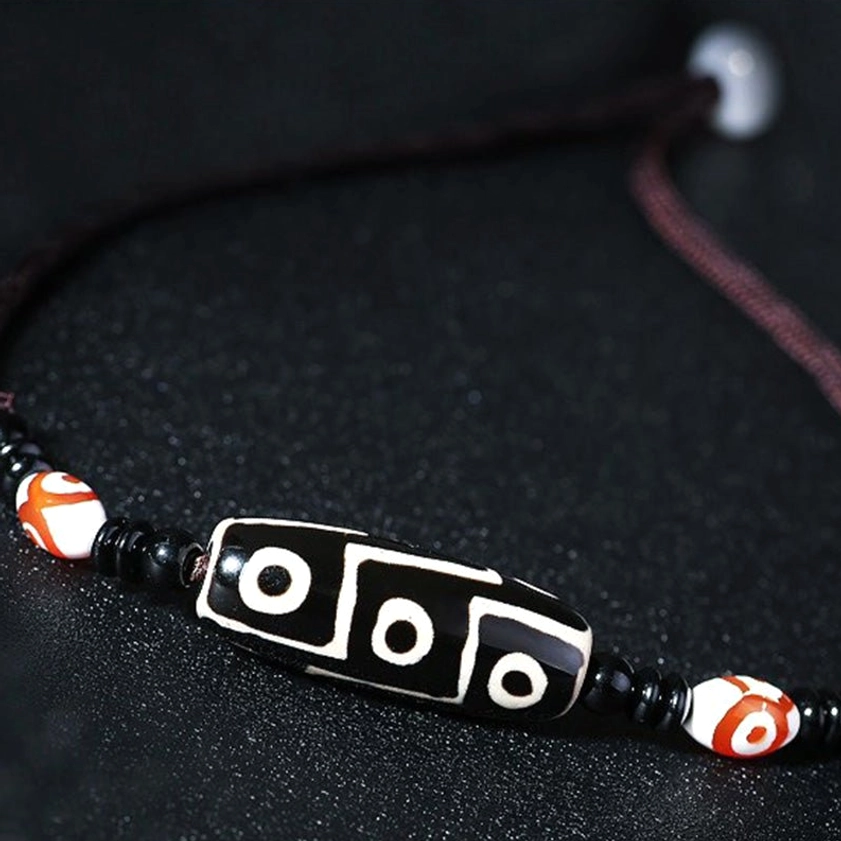 Six-eye vintage Buddhist dzi bead necklace with black braided cord and red-white spacer beads, close-up side view detail shot