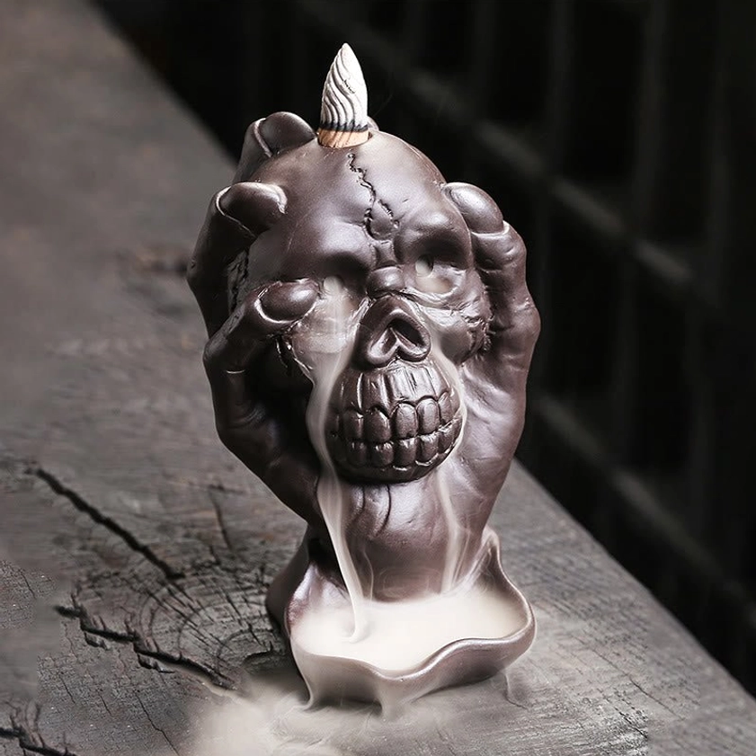 Direct front view of purple clay skull incense holder showing backflow smoke pattern and incense cone placement