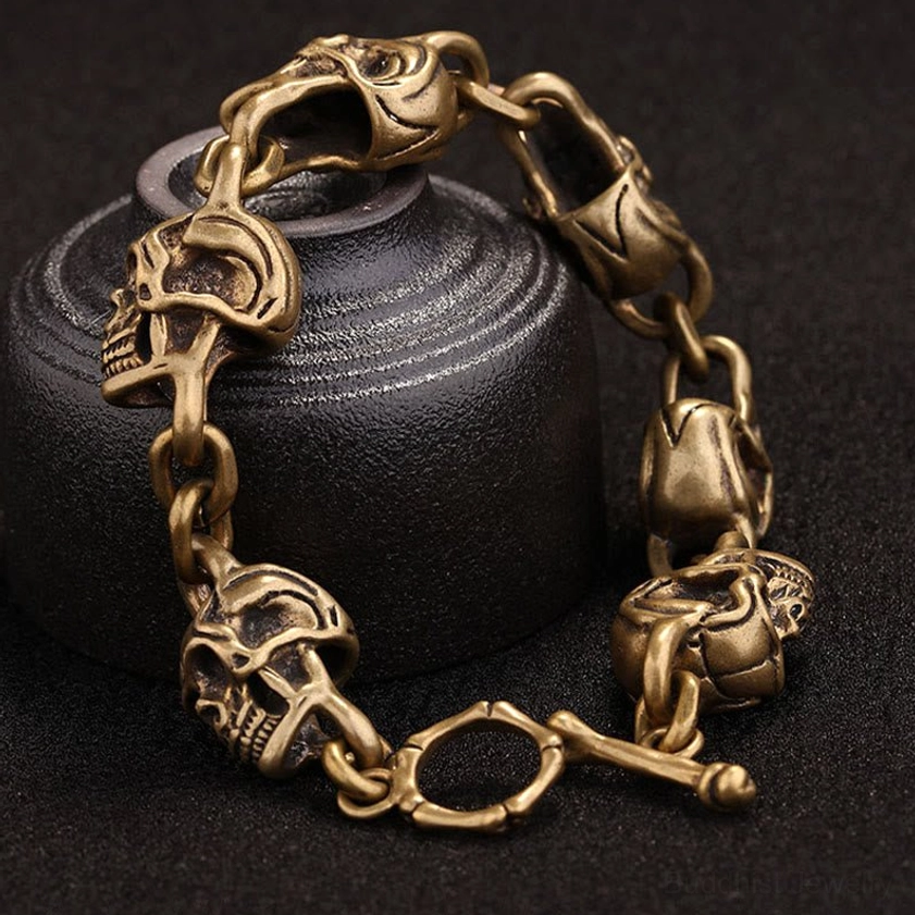 Vintage copper brass skull link bracelet with toggle clasp draped over ceramic vessel in artistic side view - handmade artisan work