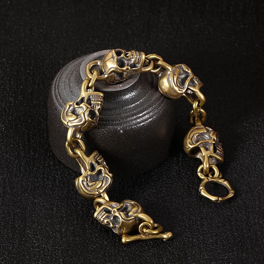 Low angle view of skull link bracelet showing curved chain with multiple carved skull charms in copper brass tone - Buddhist amulet