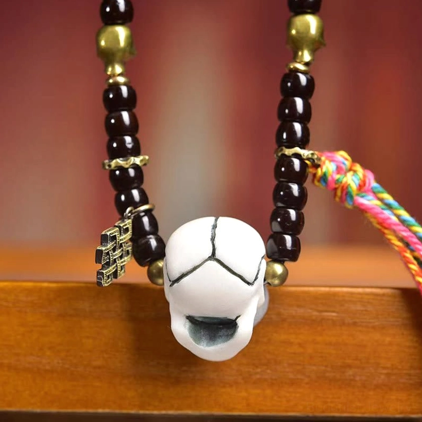 Front close-up of skull mala bracelet center pendant with brass eternal knot charm
