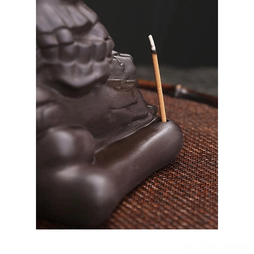 Side rear close-up of purple clay skull incense holder with stick incense inserted showing artistic carving