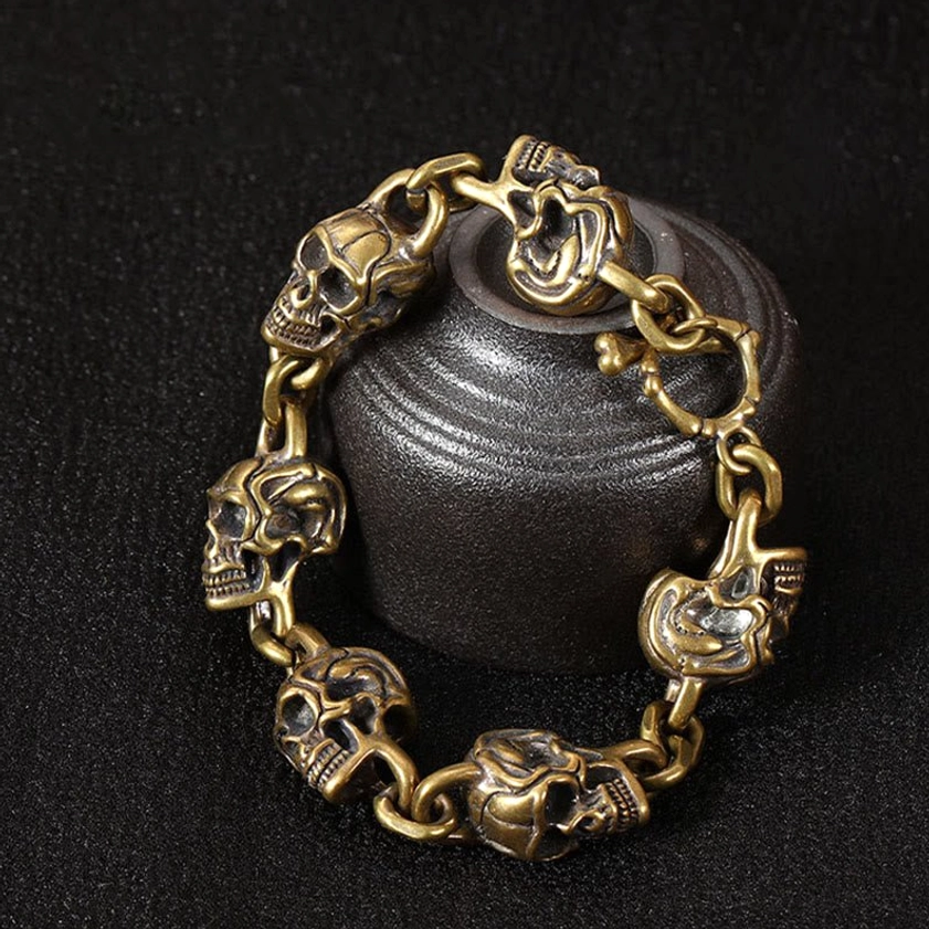 Copper brass skull bracelet draped over dark ceramic jar in oblique side view - vintage spiritual jewelry display
