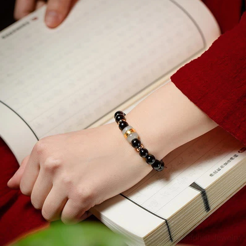 Slim black obsidian and jade beaded bracelet displayed alongside antique book and traditional red sleeve, featuring smaller black beads with gold spacers