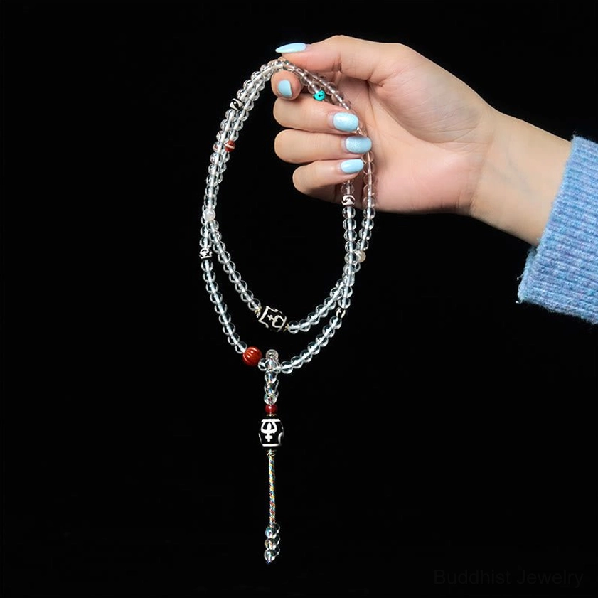 Slim crystal glass Buddhist mala with small metal dzi tassel pendant on dark background