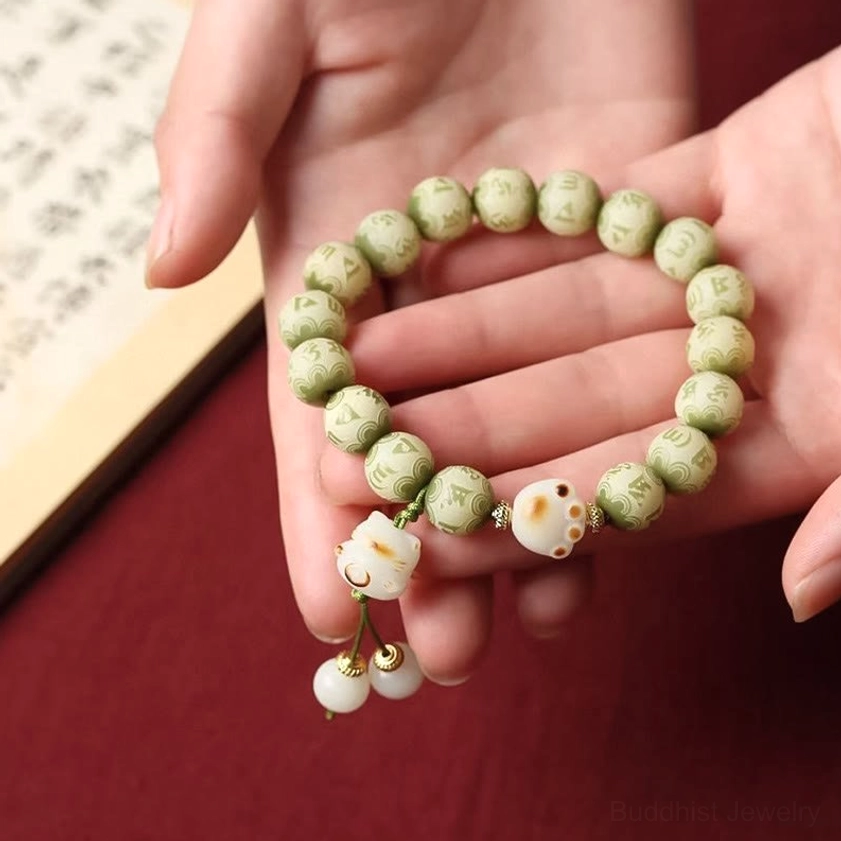 Dual-hand display of small Bodhi seed bracelet with cat paw pendants and tassel on fabric and calligraphy paper