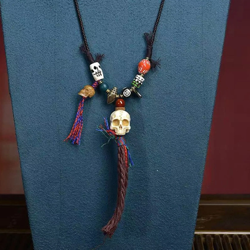 Mini bone skull Buddhist necklace with black cord, small skull charms, and decorative tassel on dark fabric background