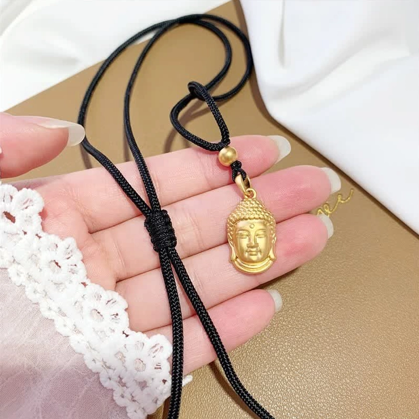 Small gold Buddha head pendant necklace worn with adjustable woven rope, handheld close-up detail shot