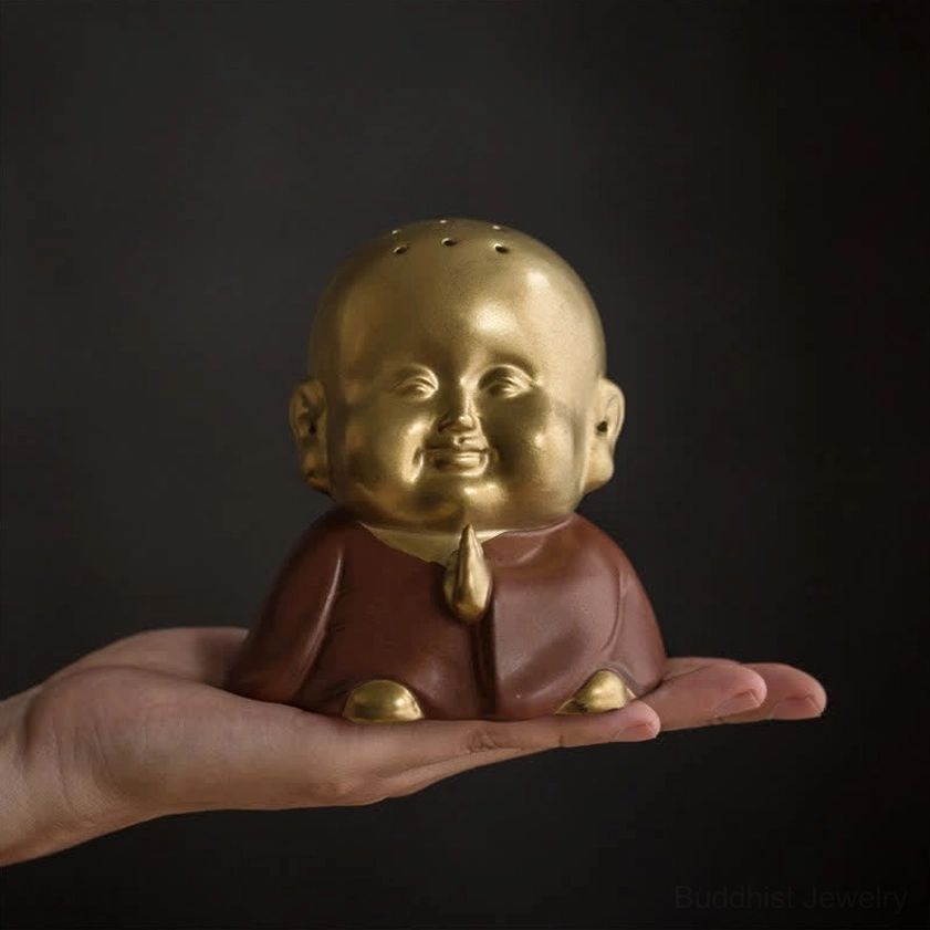 Smiling monk ceramic incense burner close-up held in palm, showing perforated head design and two-tone gold brown ceramic