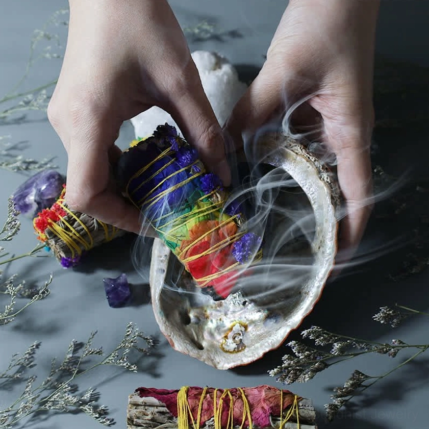 Close-up of hands holding smoking smudge stick over pearl abalone shell during sacred cleansing ritual