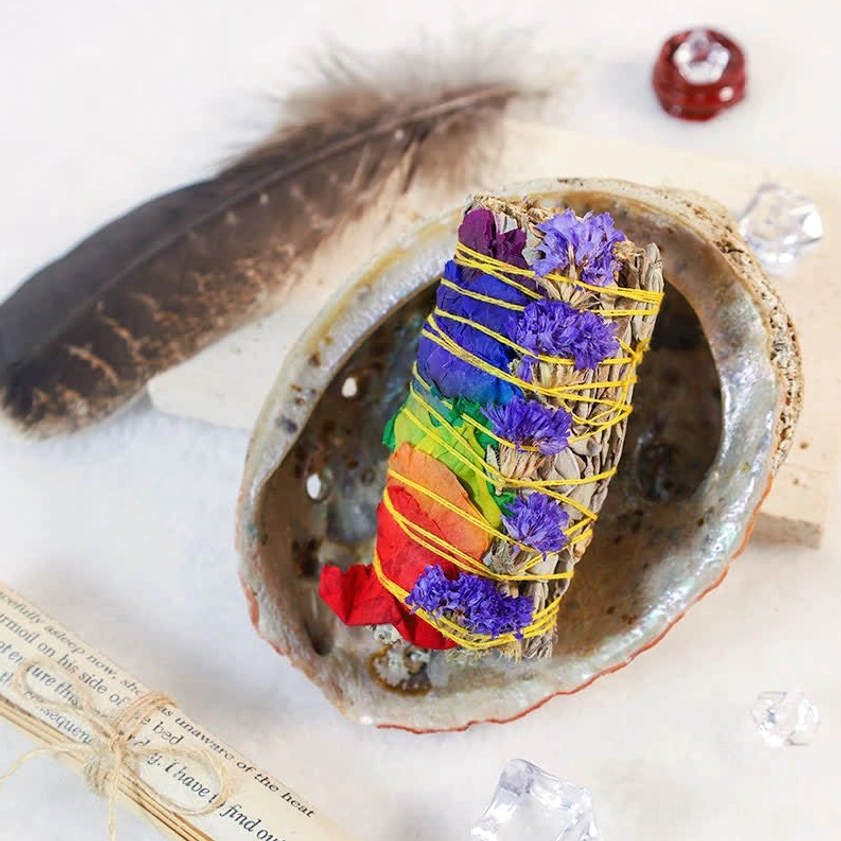 Smudge stick ritual display with abalone shell, turkey feather, and decorative crystals on tabletop
