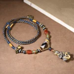 Handmade snake Buddha dzi bead necklace with braided rope and red agate beads, top-down view on wooden desk