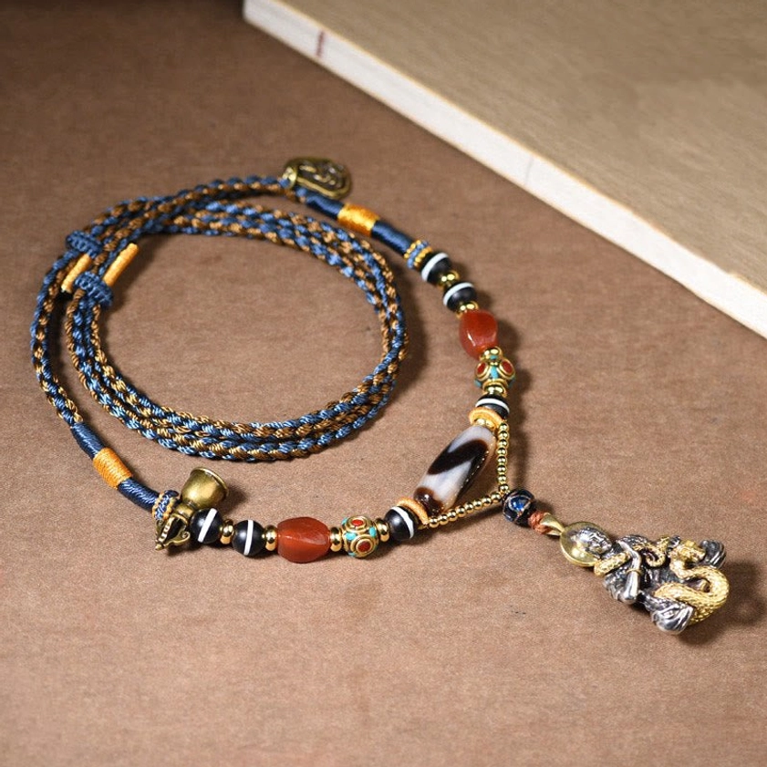Handmade snake Buddha dzi bead necklace with braided rope and red agate beads, top-down view on wooden desk