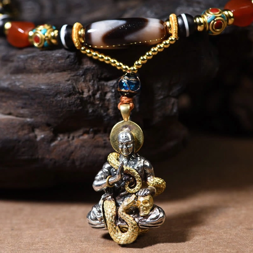 Close-up of snake Buddha necklace pendant with dual-tone gold and silver charm on dark stone background