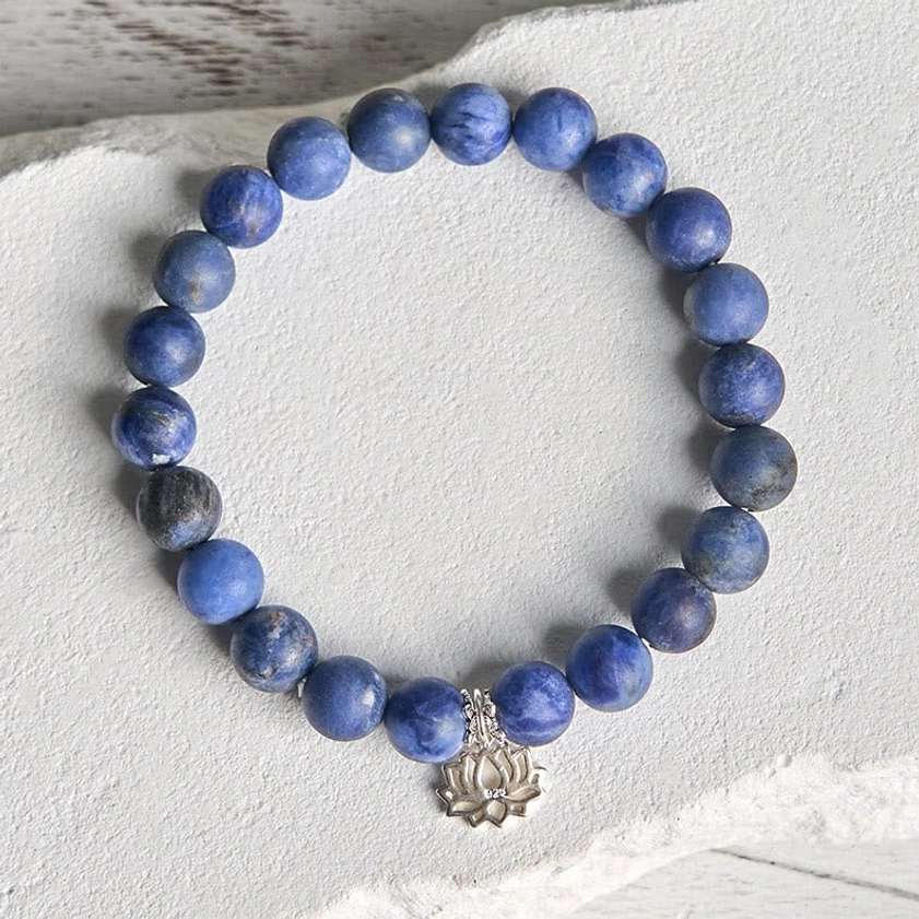 Flat lay of natural sodalite lotus bracelet with 925 sterling silver charm on textured paper surface showing bead details