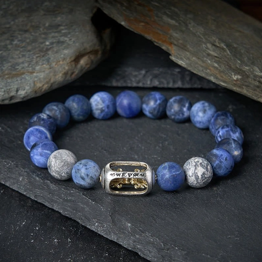 Natural stone Buddhist bracelet with sacred mantra charm displayed on slate background showing bead details