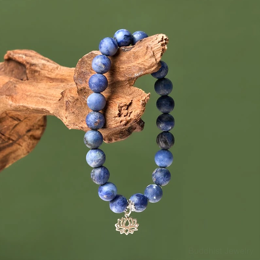 Side hanging view of sodalite lotus bracelet displayed on wooden branch with green foliage - spiritual Buddhist jewelry