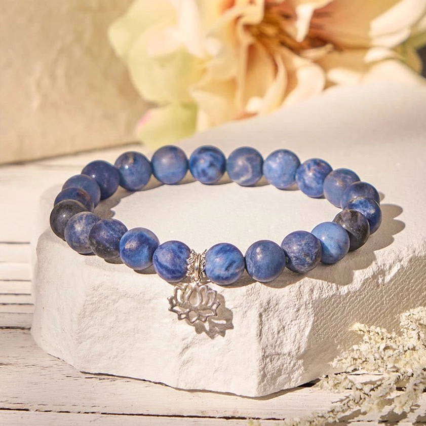 Sodalite lotus bracelet with 925 sterling silver charm displayed with natural stone and flower props - Buddhist harmony beads