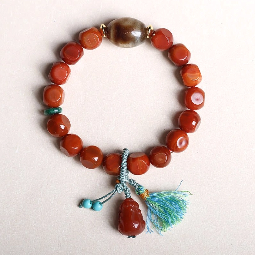 South Red Agate Pixiu fortune bracelet with faceted red beads and blue teal tassel pendant on light gray background flat lay