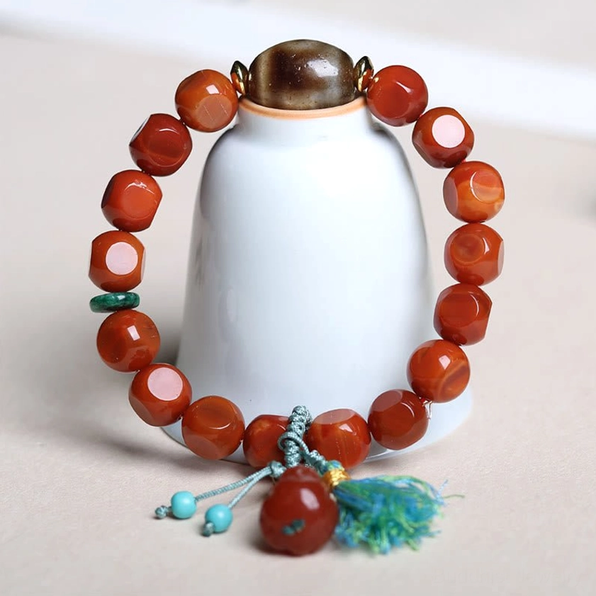 South Red Agate Pixiu fortune bracelet with faceted red beads, teal tassel, and brown central bead on white ceramic display