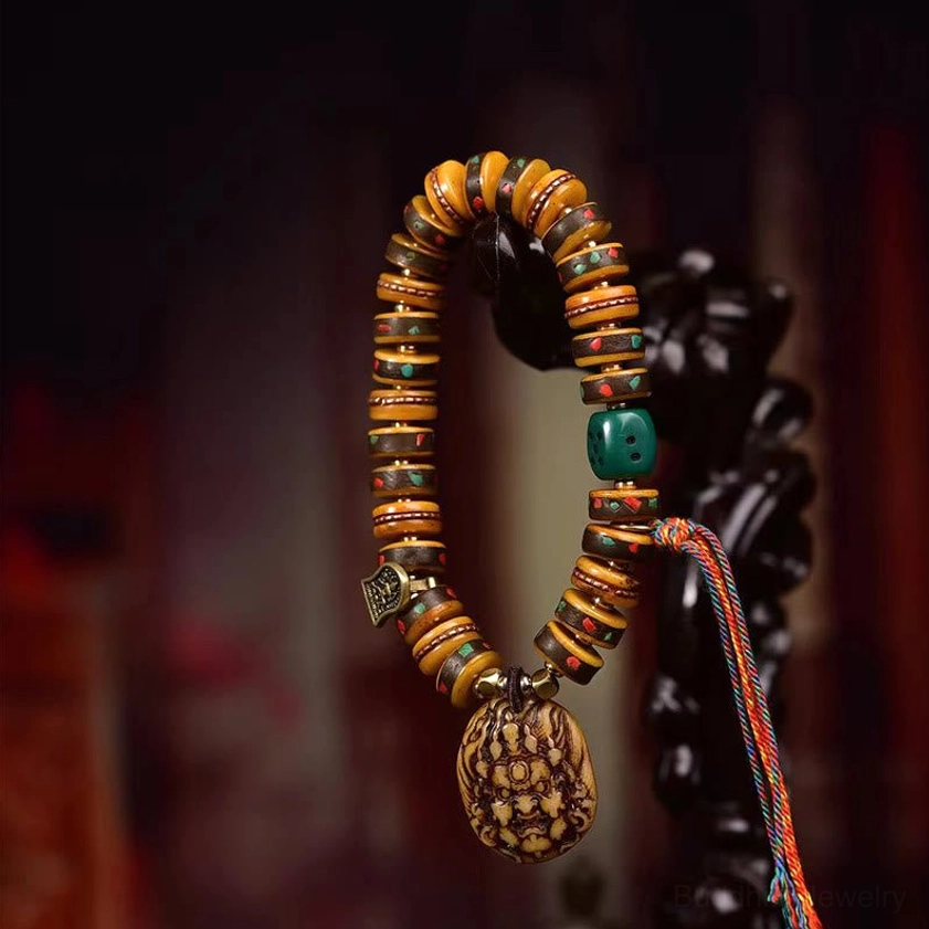 Hanging Buddhist protection bracelet with green accent bead, wrathful deity pendant, and colorful tassel cord against dark background