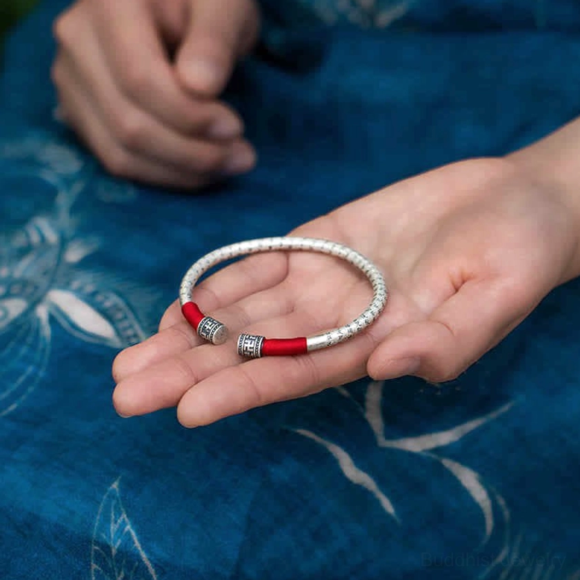 Om Mani Padme Hum silver red string bangle held in palm, showing engraved mantra details and metal accents