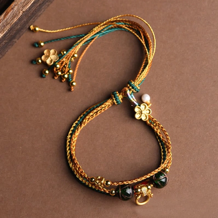 Flat-laid five elements braided bracelet featuring four-leaf clover charm, white pearl drop, and adjustable woven cord design