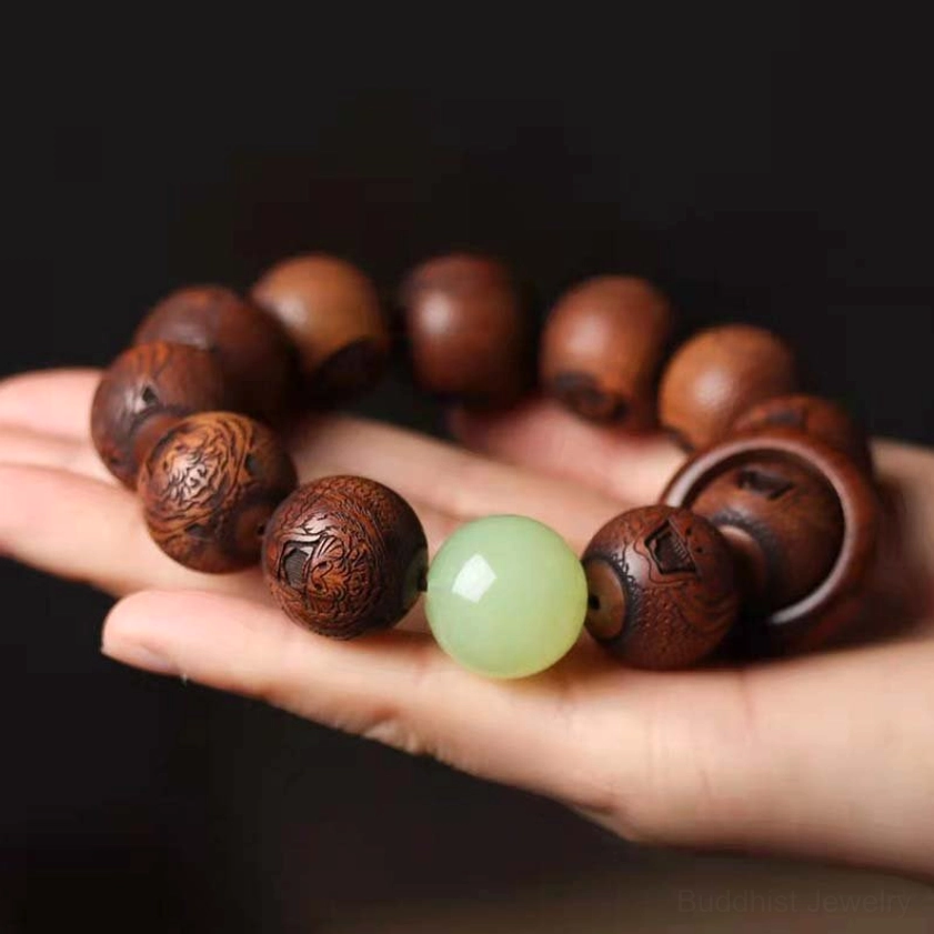Hand holding rosewood prayer bracelet overhead, showing full circular design with matte brown carved beads and jade centerpiece