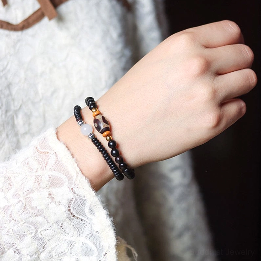 Layered stacked beaded bracelets on hand showing multiple Buddhist protection bracelets with dzi beads and wood materials worn together