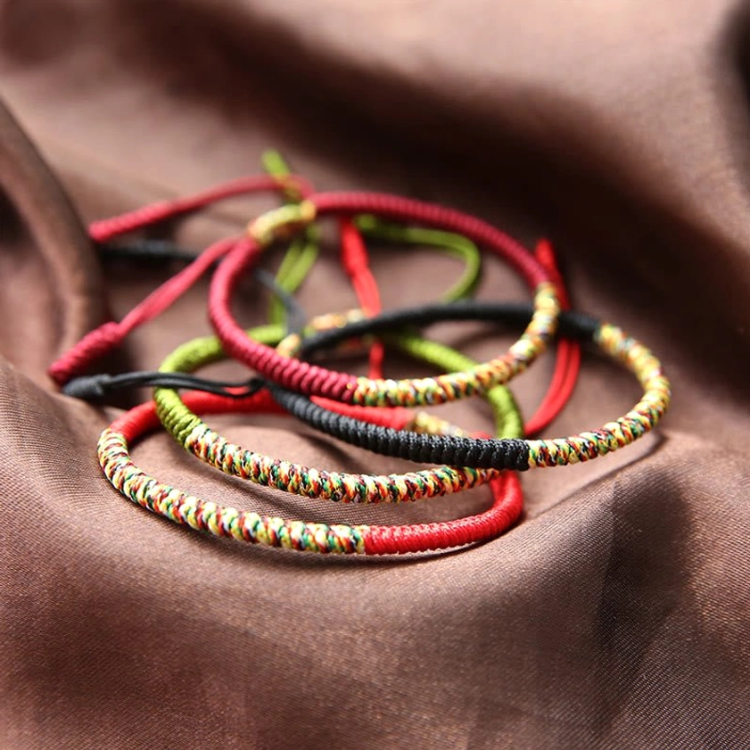 Stacked handwoven Buddhist King Kong Knot bracelets in red, black, and green with mixed braided patterns on brown satin background overhead view
