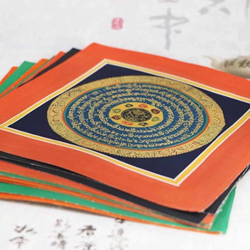 Stacked hand-painted Buddhist thangka scrolls showing orange edge borders and dark blue mandala centers – multiple authentic spiritual art pieces