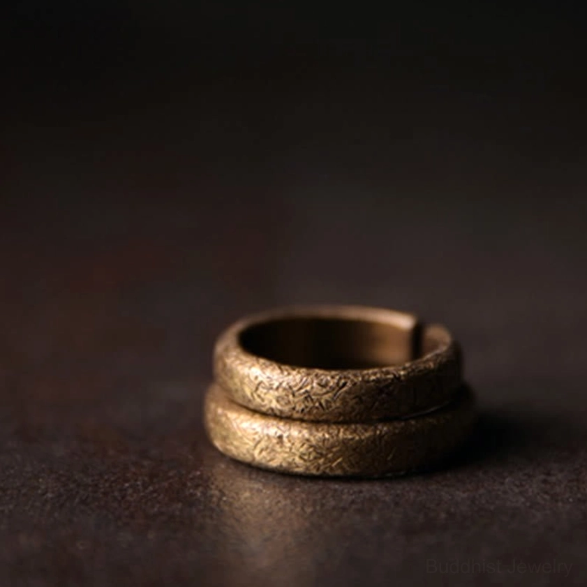 Two stacked vintage copper Buddhist rings with matching textured bronze finish, vertical side view
