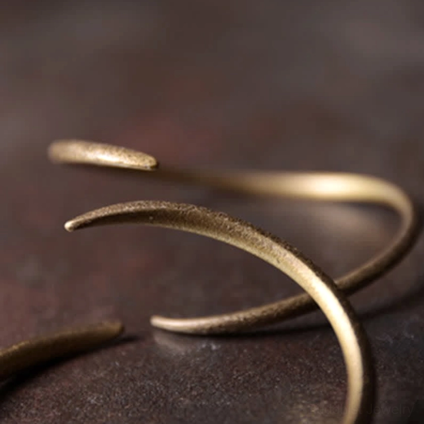 Intertwined stacked copper open cuff bracelets with textured matte gold finish on dark tabletop