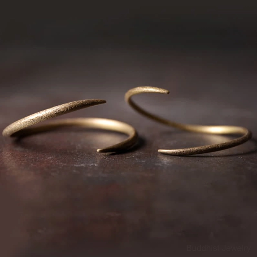 Two stacked copper cuff bracelets with hook-shaped tapered ends, matching minimalist style on brown surface