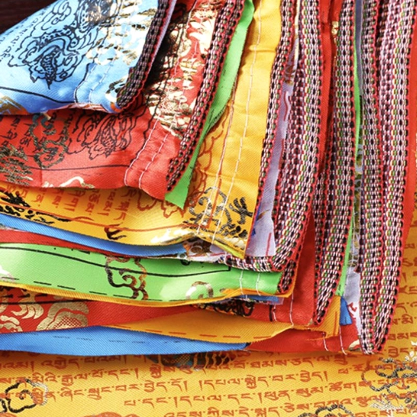 Stacked folded Buddhist prayer flags displaying colorful fabrics and woven edge details from above