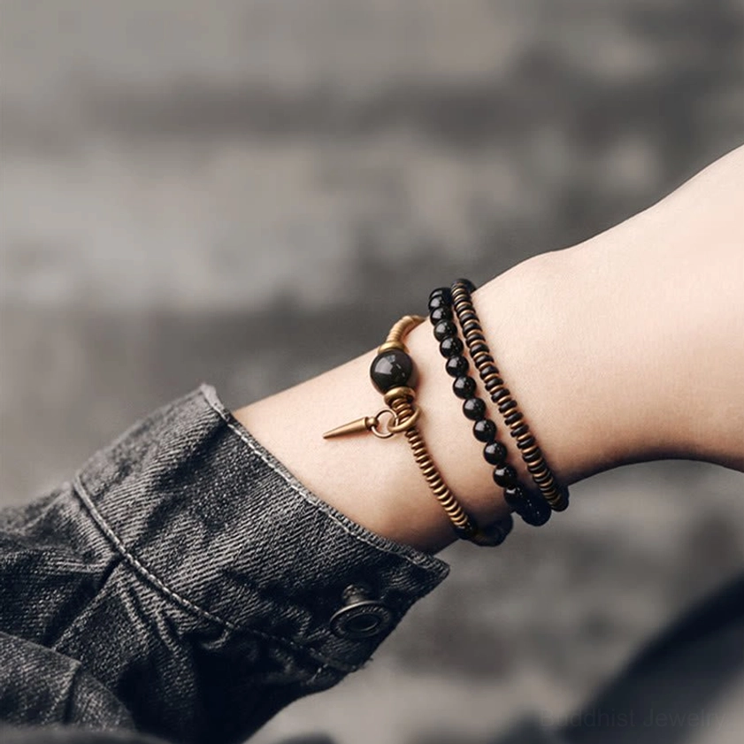 Stacked three-layer rainbow obsidian bracelet on wrist with coordinated black and bronze bead tones against denim cuff