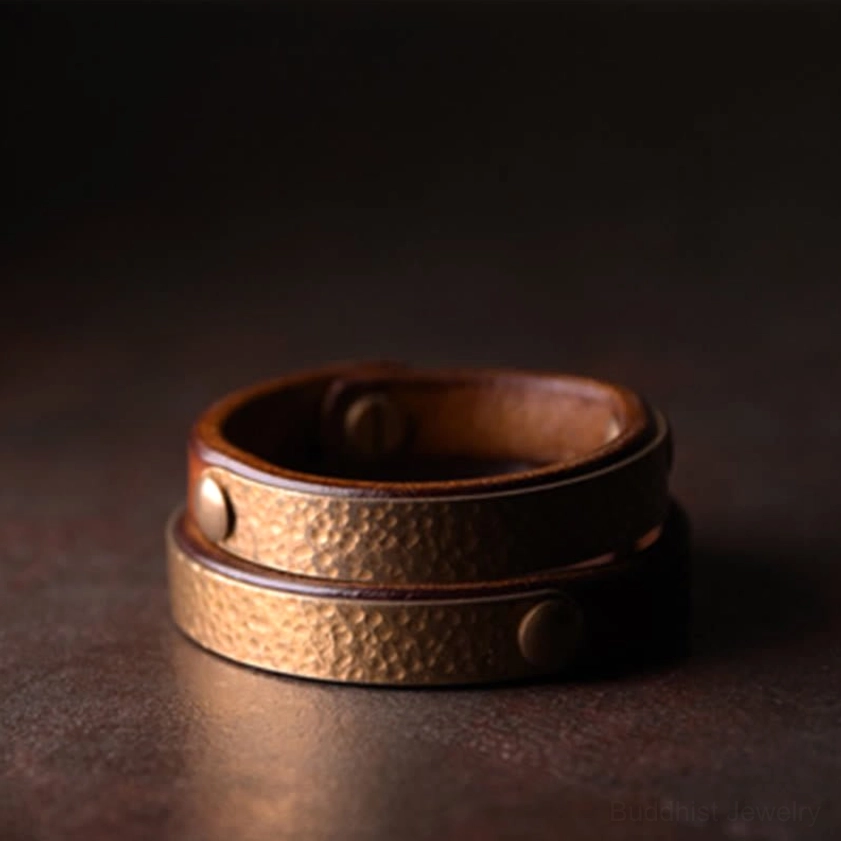 Two stacked handmade leather bangles with hammered brass design and double rivets for Buddhist prosperity