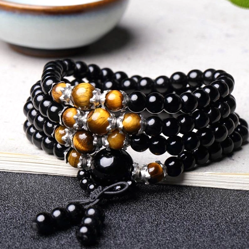 Stacked 108 bead Buddhist mala bracelet with polished glossy beads, tiger eye and silver accents on light wooden surface