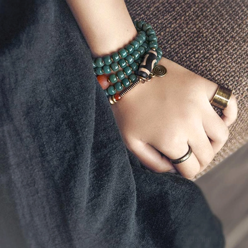 Multi-layer Buddhist mala bracelets stacked on hand with vintage metal rings showing full dzi bead ornament details
