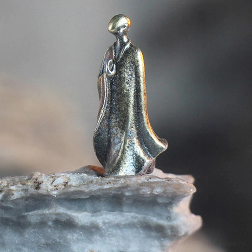 Single standing bronze Buddha figurine in prayer meditation pose with long robe on rock slab base, side eye-level view showing aged bronze patina