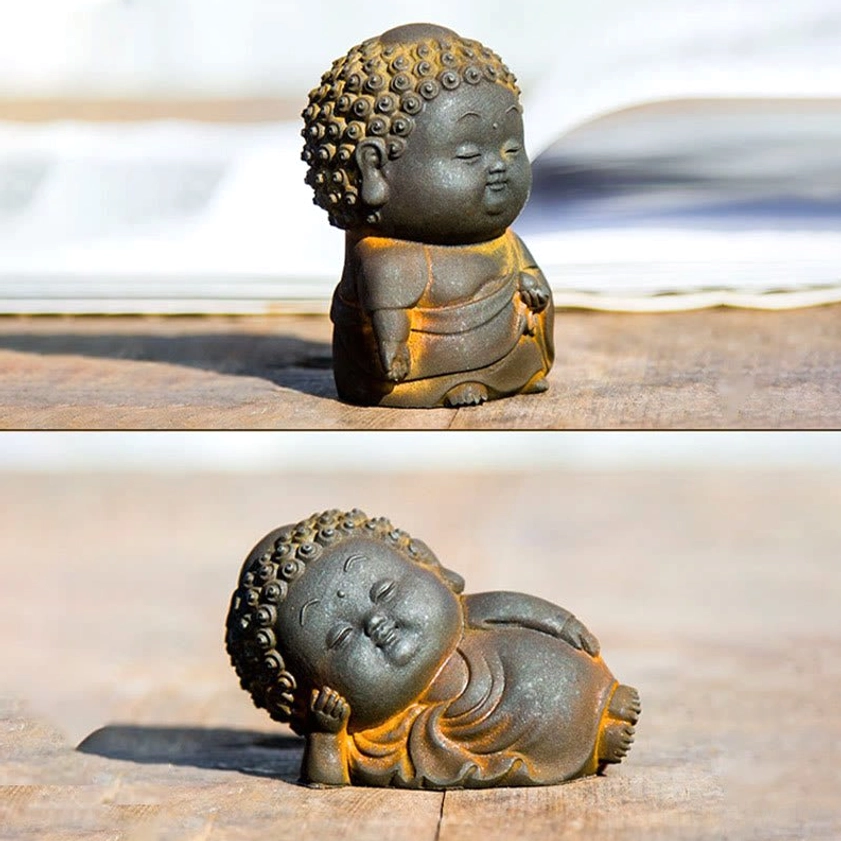 Single standing Buddha figurine with rustic dark gray finish and decorative brown trim on wooden table with book backdrop