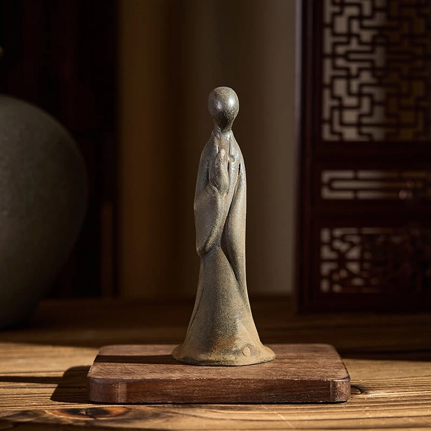 Standing Buddha statue displayed on wooden base showing side profile with aged gray-brown patina and spiritual presence