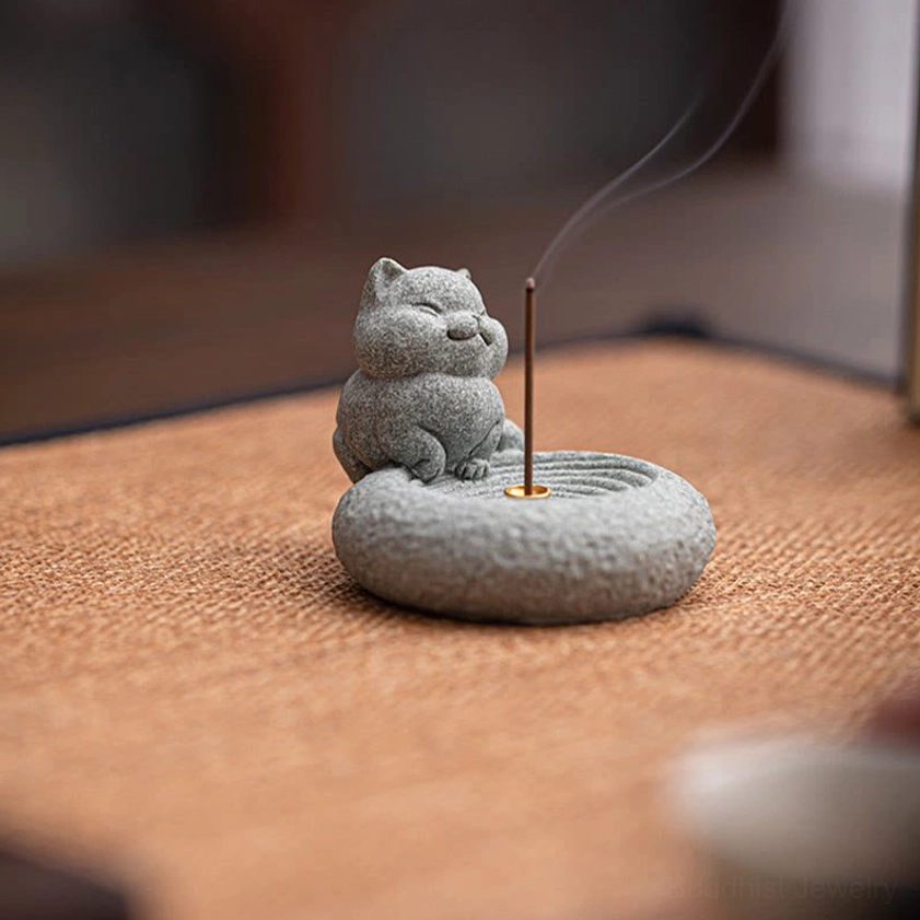 Standing cat incense holder with lit incense and smoke on woven meditation mat