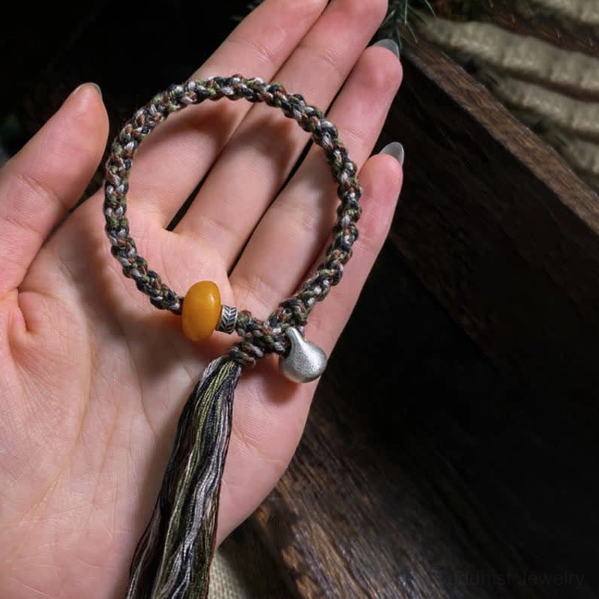 Handcrafted Buddhist protection bracelet held in palm showing multi-color woven rope and tassel