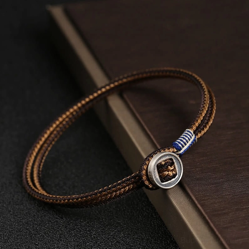 Brown woven cord Buddhist string bracelet with sterling silver metal buckle, single-strand design on dark wooden surface