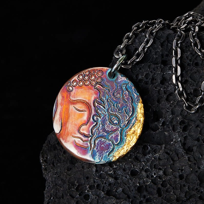 Sterling silver yin-yang Buddha demon pendant necklace with 24K gold trim displayed on volcanic stone, close-up view showing intricate dual-face engraving