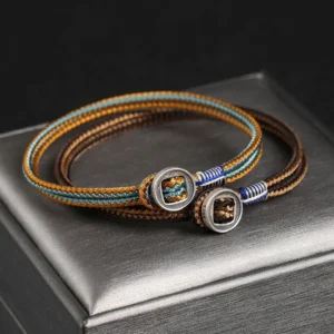 Handmade dual-strand silver string bracelet with brown blue woven cord and metal buttons, Buddhist protection design displayed on jewelry box